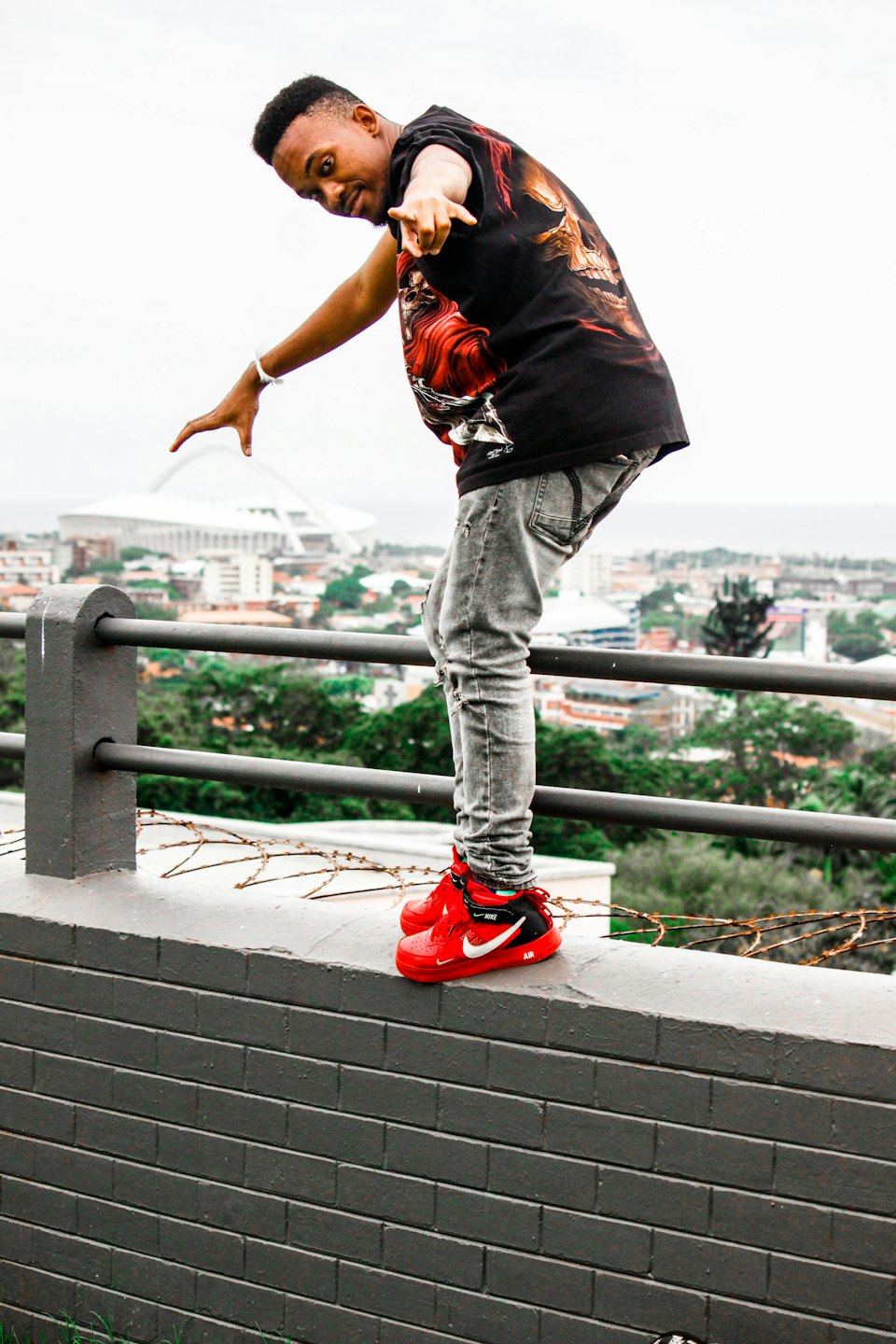 Man balancing on a brick wall points towards the viewer.